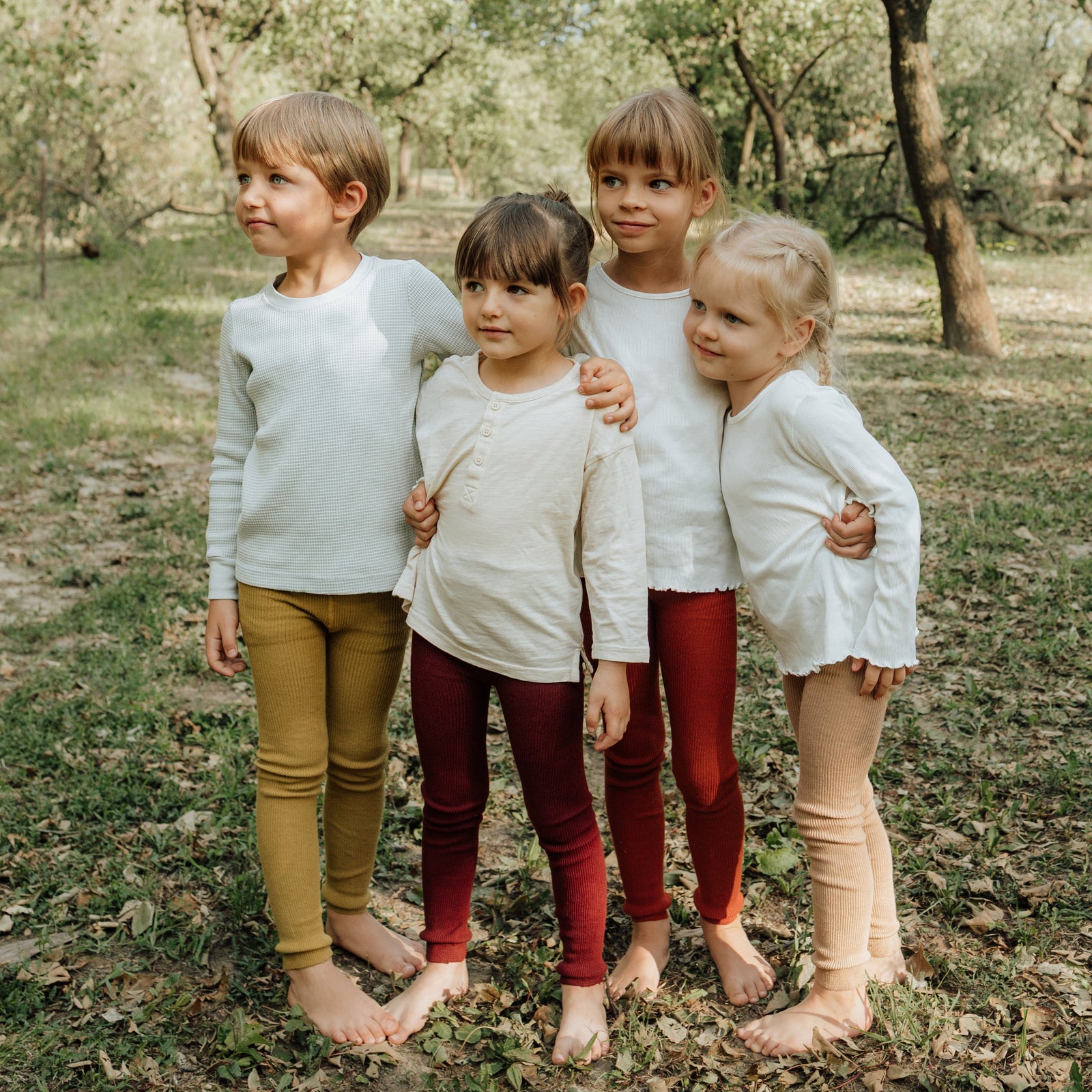 Four children wearing Peqne tights outside in a garden, posing together for a group photo.